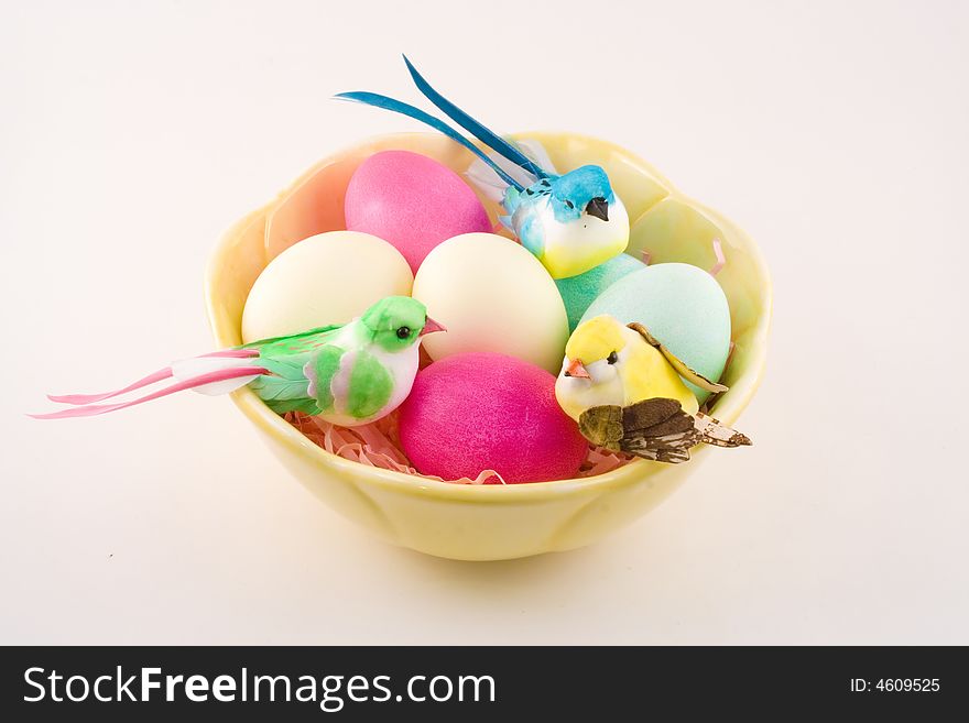 A elegant yellow bowl holds dyed Easter eggs and three pretty little birds on a light pink background. A elegant yellow bowl holds dyed Easter eggs and three pretty little birds on a light pink background.