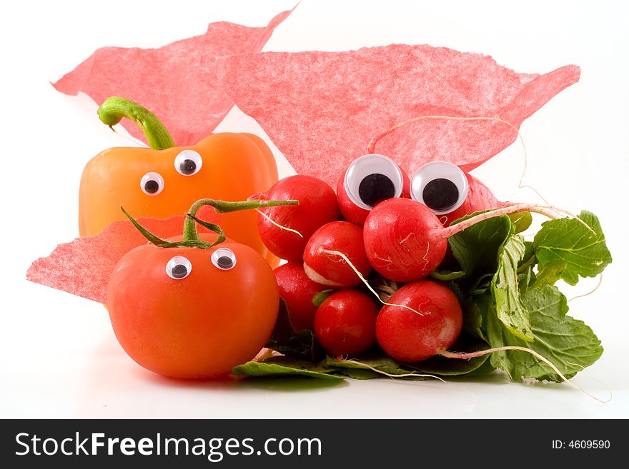 A bunch of radishes, a tomato and an orange bell pepper with googly eyes and red capes sit on a white background. A bunch of radishes, a tomato and an orange bell pepper with googly eyes and red capes sit on a white background.