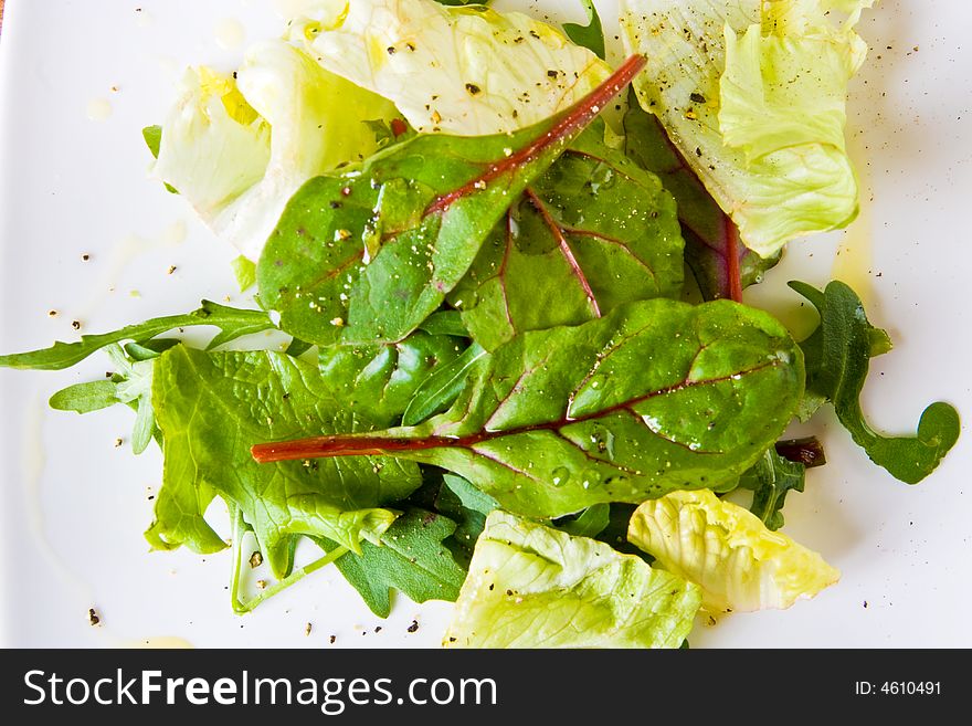 Green salad leaves with pepper and olive oil on a white plate