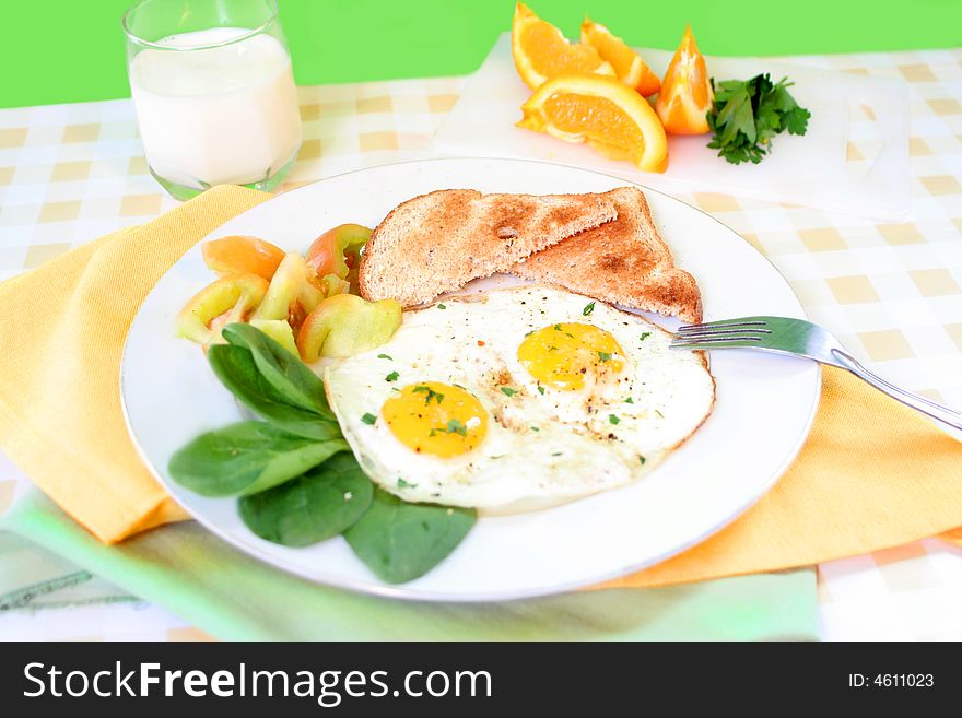 Two sunny side up eggs on plate with fresh vegetables whole wheat toast and sliced orange in the background. Two sunny side up eggs on plate with fresh vegetables whole wheat toast and sliced orange in the background