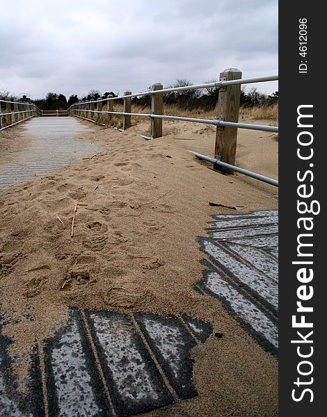 Fence leading down a sandy boardwalk on a beach.