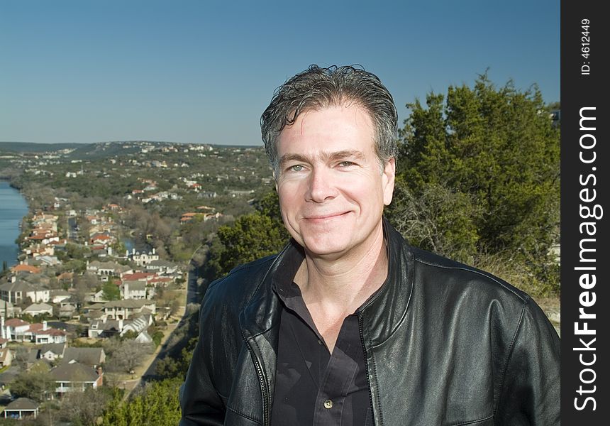 A smiling man on a hilltop with an affluential riverside neighborhood in the valley below him. A smiling man on a hilltop with an affluential riverside neighborhood in the valley below him.