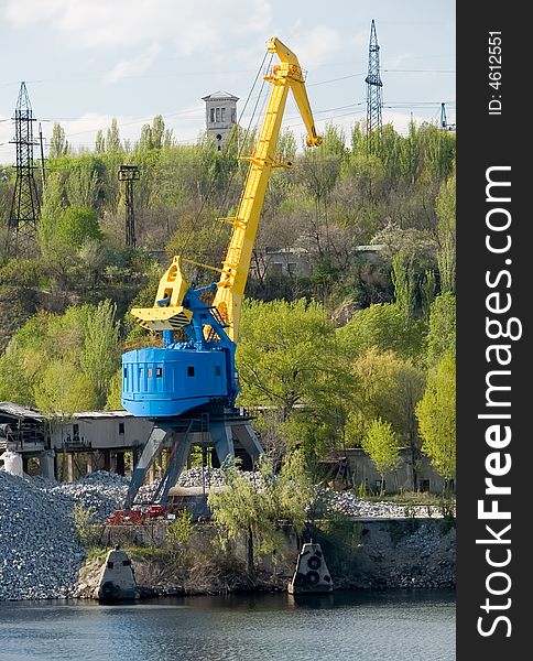 Yellow port crane on a river bank ready to load rocks. Yellow port crane on a river bank ready to load rocks