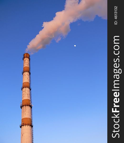 Factory pipe smoking with a white smoke and a moon nearby over the blue sky. Factory pipe smoking with a white smoke and a moon nearby over the blue sky