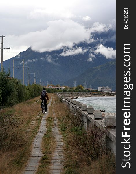 A man cycling by the riverside in deep valley - Tibet-china. A man cycling by the riverside in deep valley - Tibet-china.