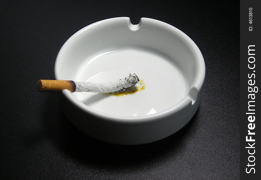 The burned down cigarette in a white ashtray on a black background