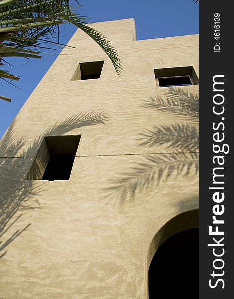 The wall of an arabian house in sunlight with gentle shadows from surounding palm trees. The wall of an arabian house in sunlight with gentle shadows from surounding palm trees