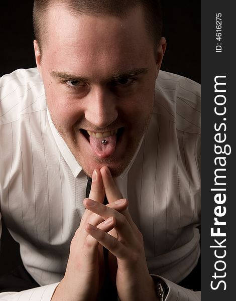 Portrait of a young businessman with tongue piercing on dark background