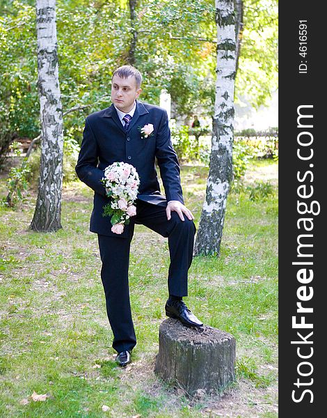 Groom with a flower bouquet waits for his bride in the park. Groom with a flower bouquet waits for his bride in the park