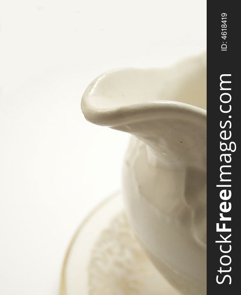 Image of an old white creamer with a floral design, with focus on the spout.  White background and vertical orientation. Image of an old white creamer with a floral design, with focus on the spout.  White background and vertical orientation.