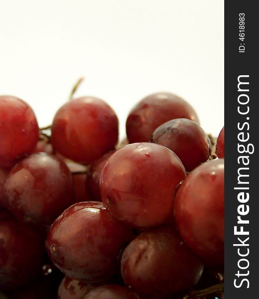 Close up image of piled wet red grapes, on white background.  Vertical orientation.