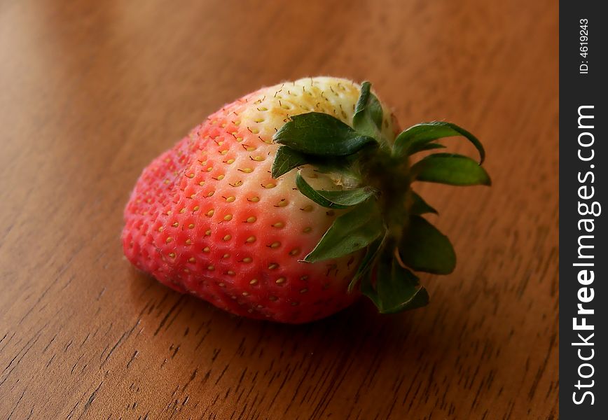 Image of a single red and white strawberry on a wooden surface, in natural sunlight.  Horizontal orientation. Image of a single red and white strawberry on a wooden surface, in natural sunlight.  Horizontal orientation.