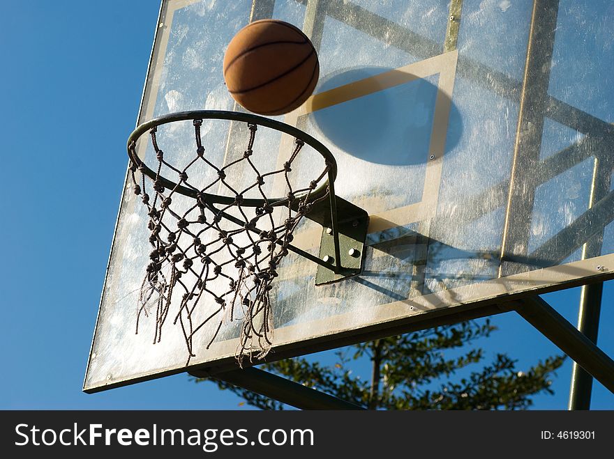 Basketball dropping into the net in a basketball game on an open court at sunset. Basketball dropping into the net in a basketball game on an open court at sunset