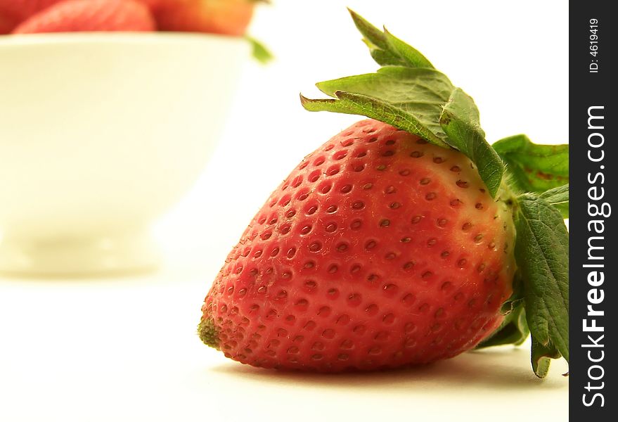 Close up image of a large red strawberry, with other strawberries in a bowl in the background.  White background and horizontal orientation. Close up image of a large red strawberry, with other strawberries in a bowl in the background.  White background and horizontal orientation.
