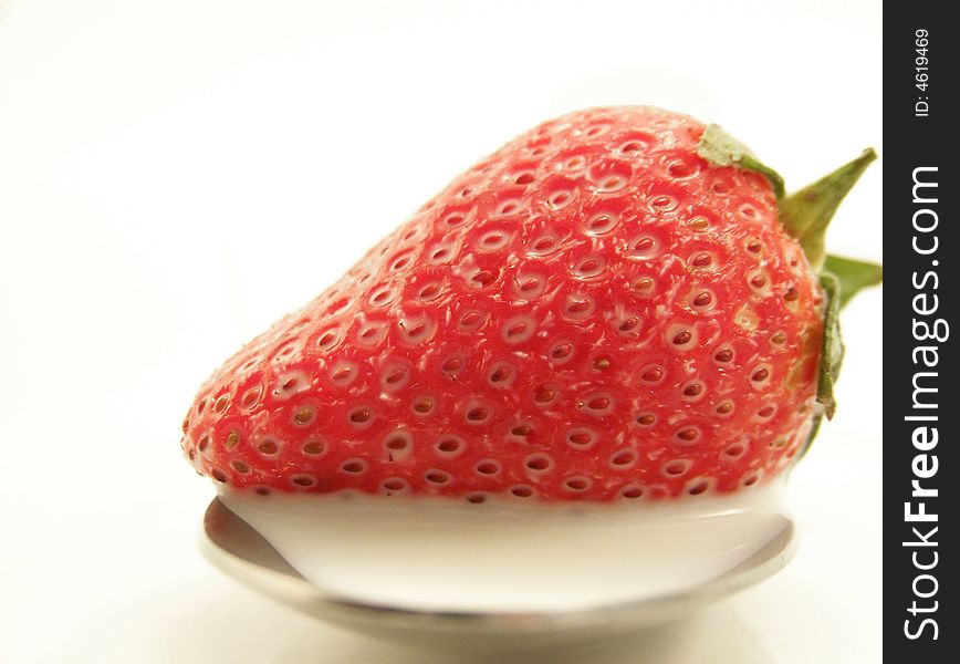 Image of a bright red strawberry on a spoon with white milk.  White background.  Vertical orientation. Image of a bright red strawberry on a spoon with white milk.  White background.  Vertical orientation.
