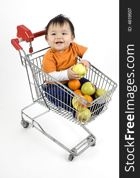 Baby sitting in a shopping cart with fruit before white 
background. Baby sitting in a shopping cart with fruit before white 
background