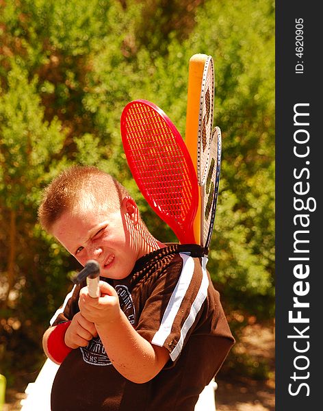 Young boy pretending that he is shooting at photographer with tennis rackets as additional ammo stuffed down the back of his shirt. Young boy pretending that he is shooting at photographer with tennis rackets as additional ammo stuffed down the back of his shirt.