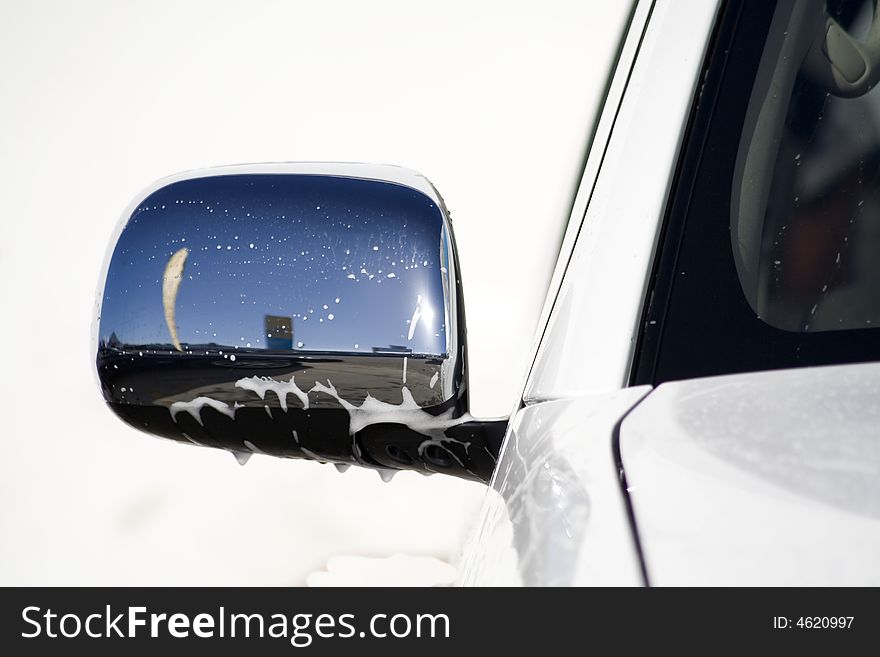 A reflection of the blue sky and a flag in chrome rear-view mirror of a car. A reflection of the blue sky and a flag in chrome rear-view mirror of a car.
