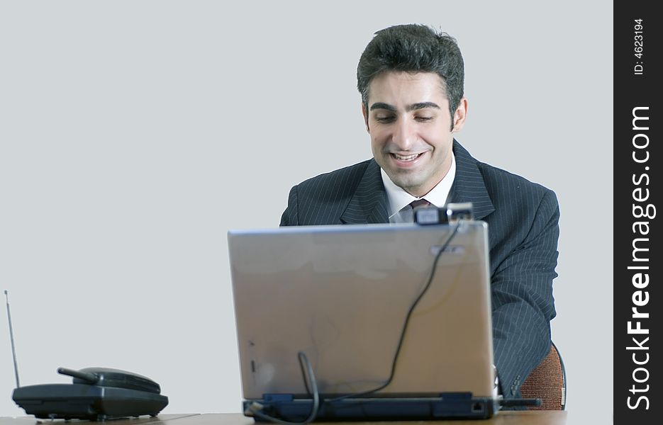 Business man working at his laptop and smiling. Isolated against a grey background. Business man working at his laptop and smiling. Isolated against a grey background