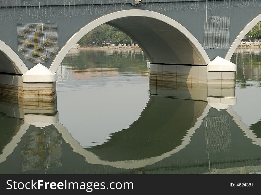 Curved arches under a bridge with its reflection in the still waters of the river. Curved arches under a bridge with its reflection in the still waters of the river