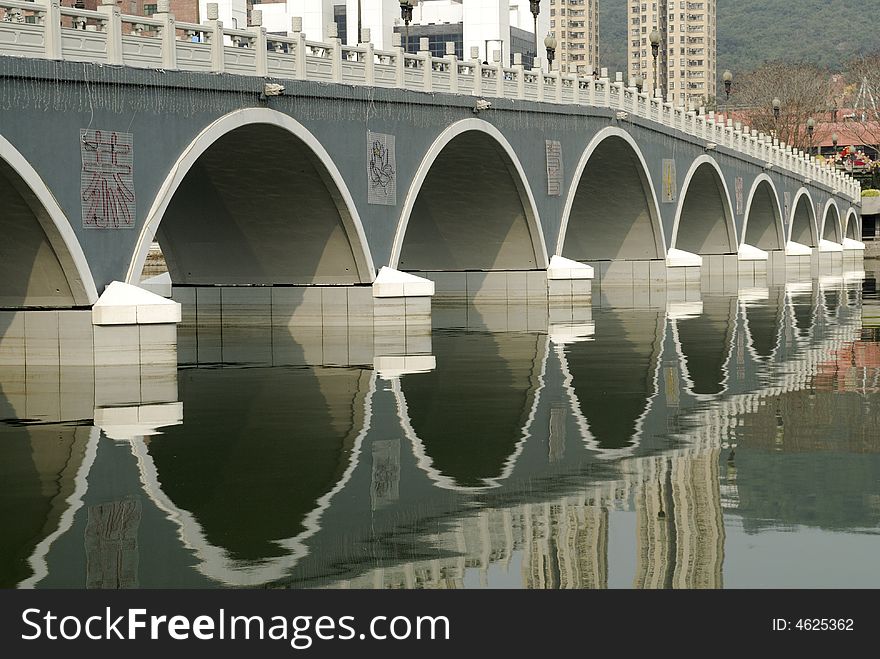 Curved arches under a bridge with its reflection in the still waters of the river. Curved arches under a bridge with its reflection in the still waters of the river
