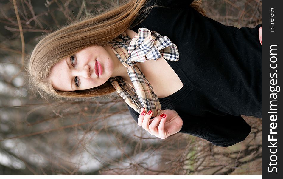 Thoughtful young girl in a black sweater a hand corrects for a scarf in a cell