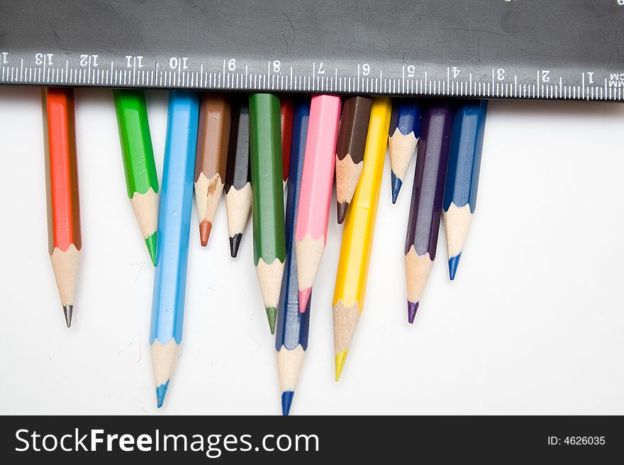 Multicolored pencils and black ruller on the whie isolated background. Multicolored pencils and black ruller on the whie isolated background