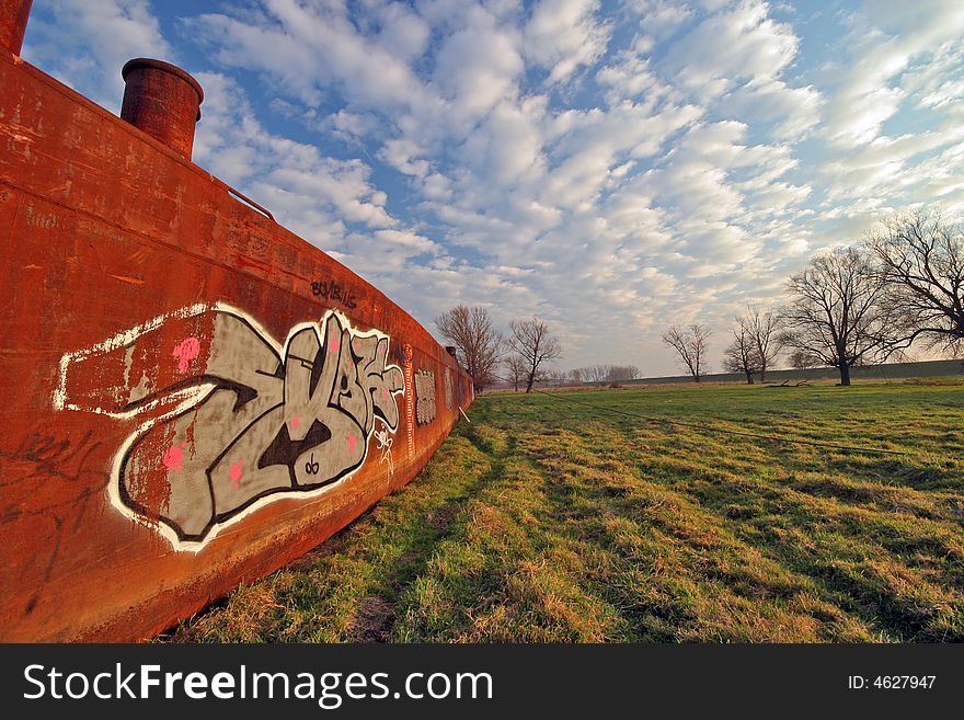 Old rusty boat on meadow with cloudy sky
