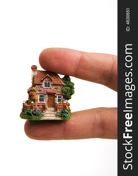 A small porcelain figurine of a country house between human fingers. A small porcelain figurine of a country house between human fingers.