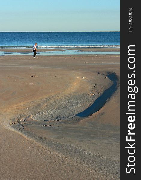 A person walking along the water's edge in the early morning. Deeply sculpured sand patterns create foreground interest. A person walking along the water's edge in the early morning. Deeply sculpured sand patterns create foreground interest