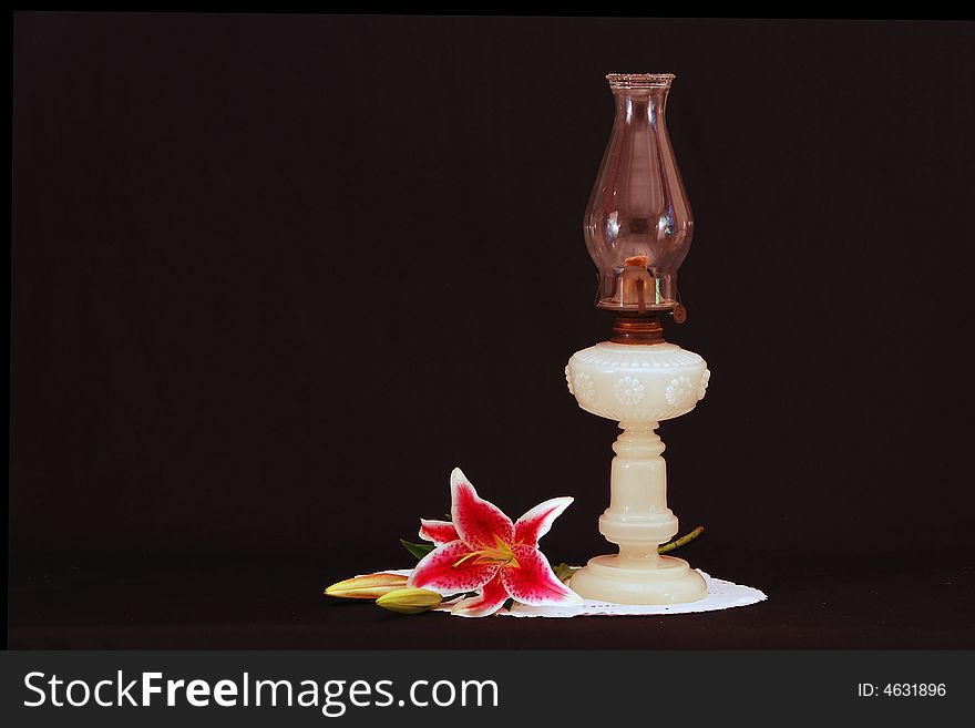 A milk glass oil lanp from the late 1800s. It has a decorative around the bowl, mantle and wick turner. Ared lily complements the composition. A milk glass oil lanp from the late 1800s. It has a decorative around the bowl, mantle and wick turner. Ared lily complements the composition