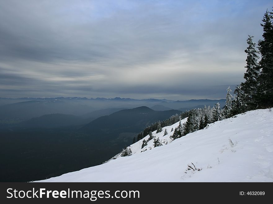 View onto green pine covered hills from a snow covered slope. View onto green pine covered hills from a snow covered slope