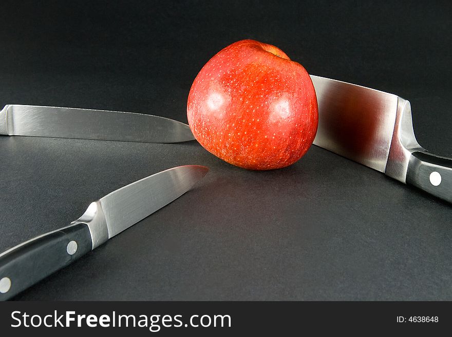 Bright red apple on dark background and three kitchen knives. Bright red apple on dark background and three kitchen knives