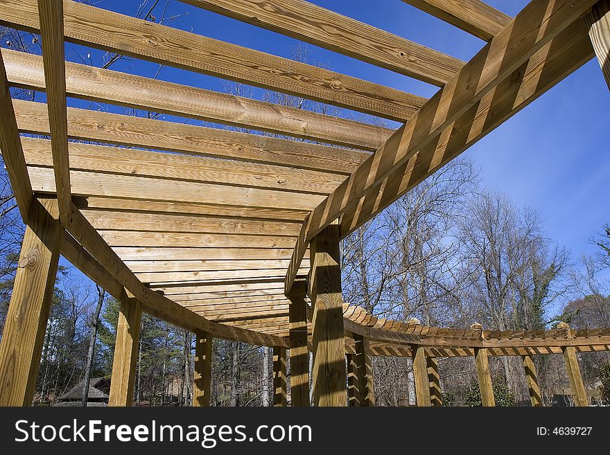 A curving wood structure hanging over a walkway in the park. A curving wood structure hanging over a walkway in the park