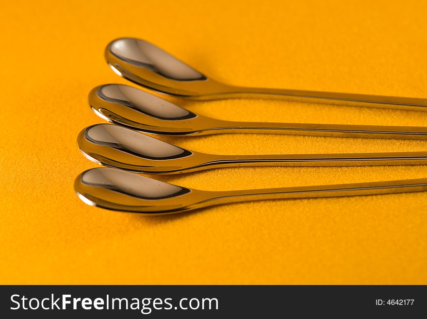 Four tea spoons making a pattern against a yellow background