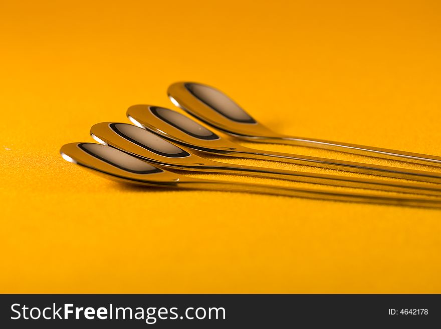 Four tea spoons making a pattern against a yellow background