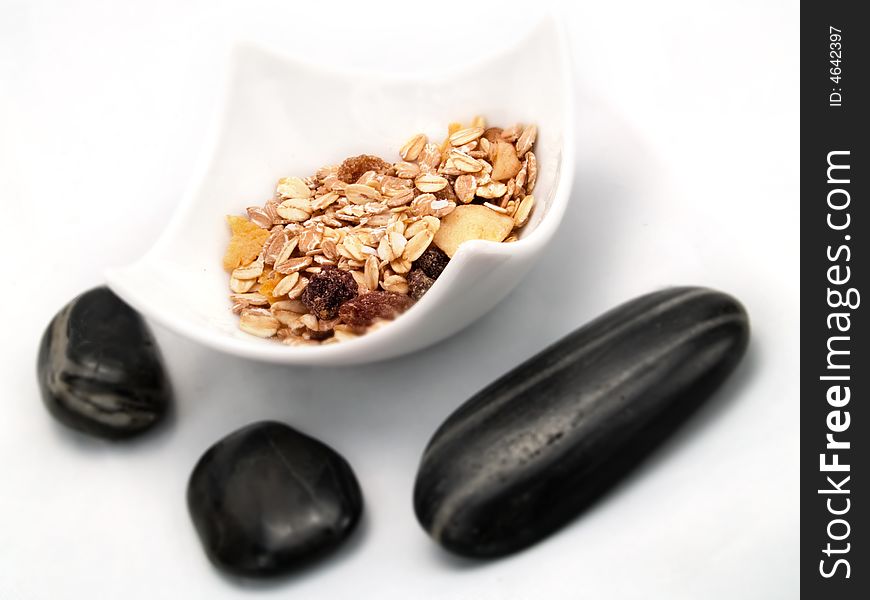 Several cereals in a white bowl, and some dark ying-yang stones