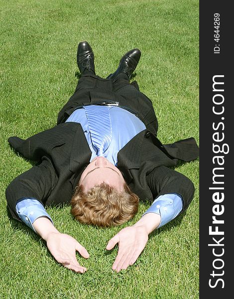 Single white businessman in suit stretches and relaxes on green grass. Single white businessman in suit stretches and relaxes on green grass