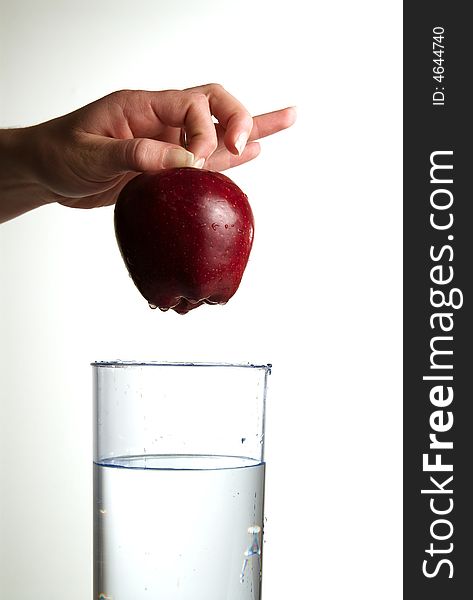 A hand dropping an apple in glass water. A hand dropping an apple in glass water