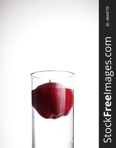 Glass of water and red apple floating in it.