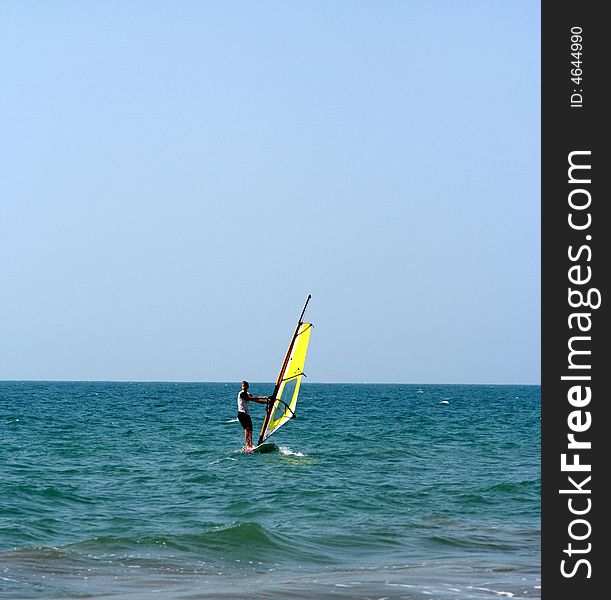 A yellow windsurfer and sailboad on the sea. A yellow windsurfer and sailboad on the sea
