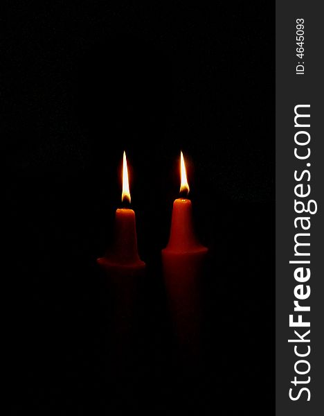 Two candles light in darkness