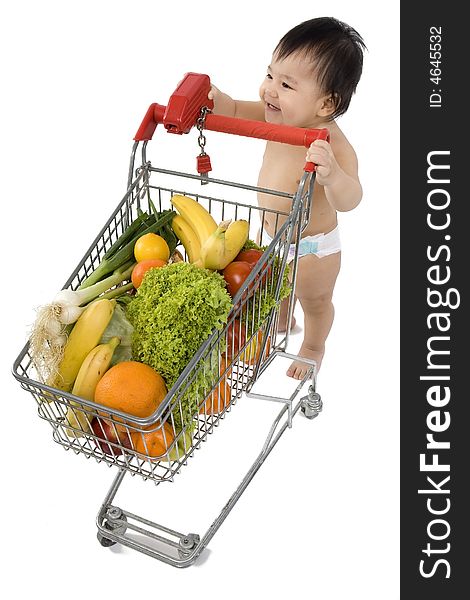 Baby pushes a shopping cart with fruits and vegetables before a white background. Baby pushes a shopping cart with fruits and vegetables before a white background