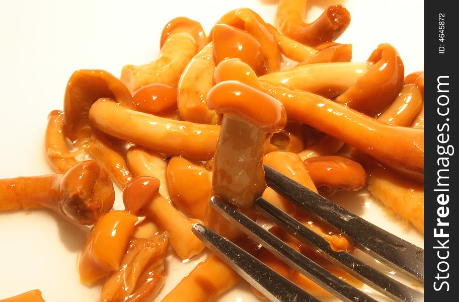 Close-up of steel fork with marinaded honey fungus on background with mushrooms. Close-up of steel fork with marinaded honey fungus on background with mushrooms