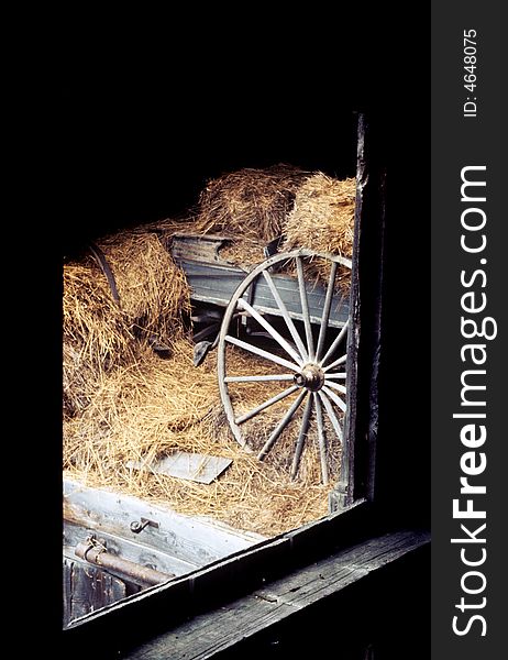 An old cart wheel sitting in a barn surrounded by hay. An old cart wheel sitting in a barn surrounded by hay