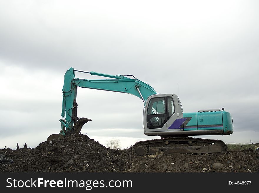 A backhoe Excavator digging in the dirt and debris with white clouds in the background. This is a great excavation, construction background with plenty of copy space. A backhoe Excavator digging in the dirt and debris with white clouds in the background. This is a great excavation, construction background with plenty of copy space