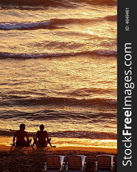 Photo of beautiful sunset, two friends seating on the beach