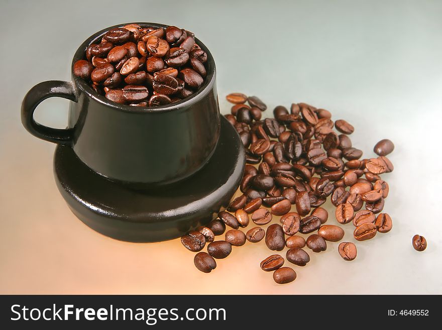 Coffee beans of two kind in a little brown cup and saucer on color background from glass. Coffee beans of two kind in a little brown cup and saucer on color background from glass