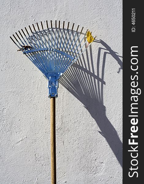 A rake standing against a white wall in the sun. A rake standing against a white wall in the sun.
