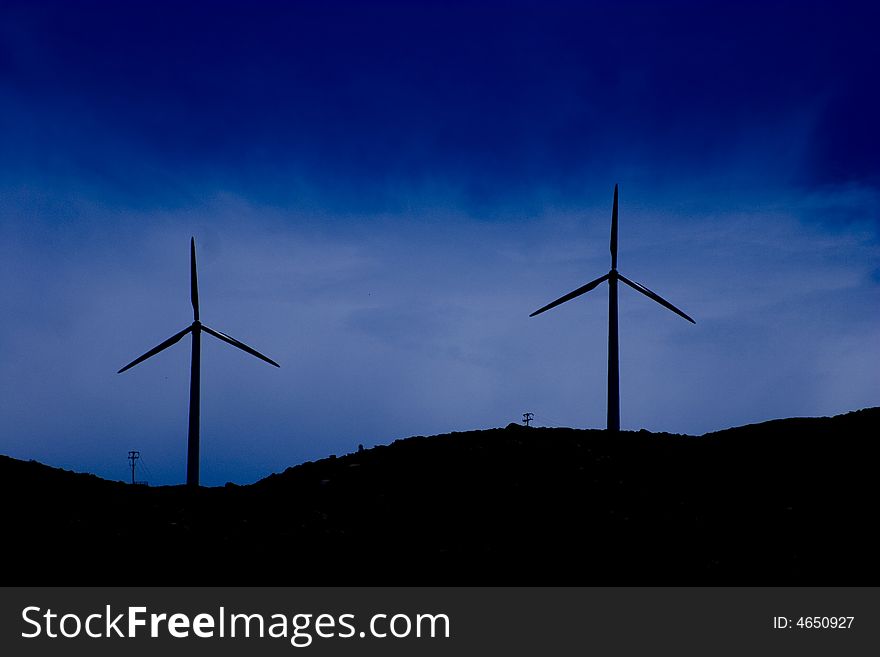 Silhouette of two wind turbines on a hill top. Silhouette of two wind turbines on a hill top